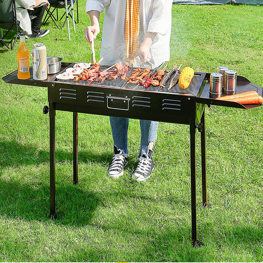 Black Outdoor Portable Charcoal Barbecue Grill with Dual Prep Panels in Garden Setting – Ideal for Camping and Outdoor Cooking
